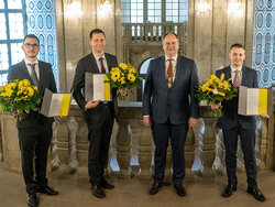 three of the four award winners and mayor Hilbert stand beside each other. Each award winner holds a bouquet of flowers and the certificate.